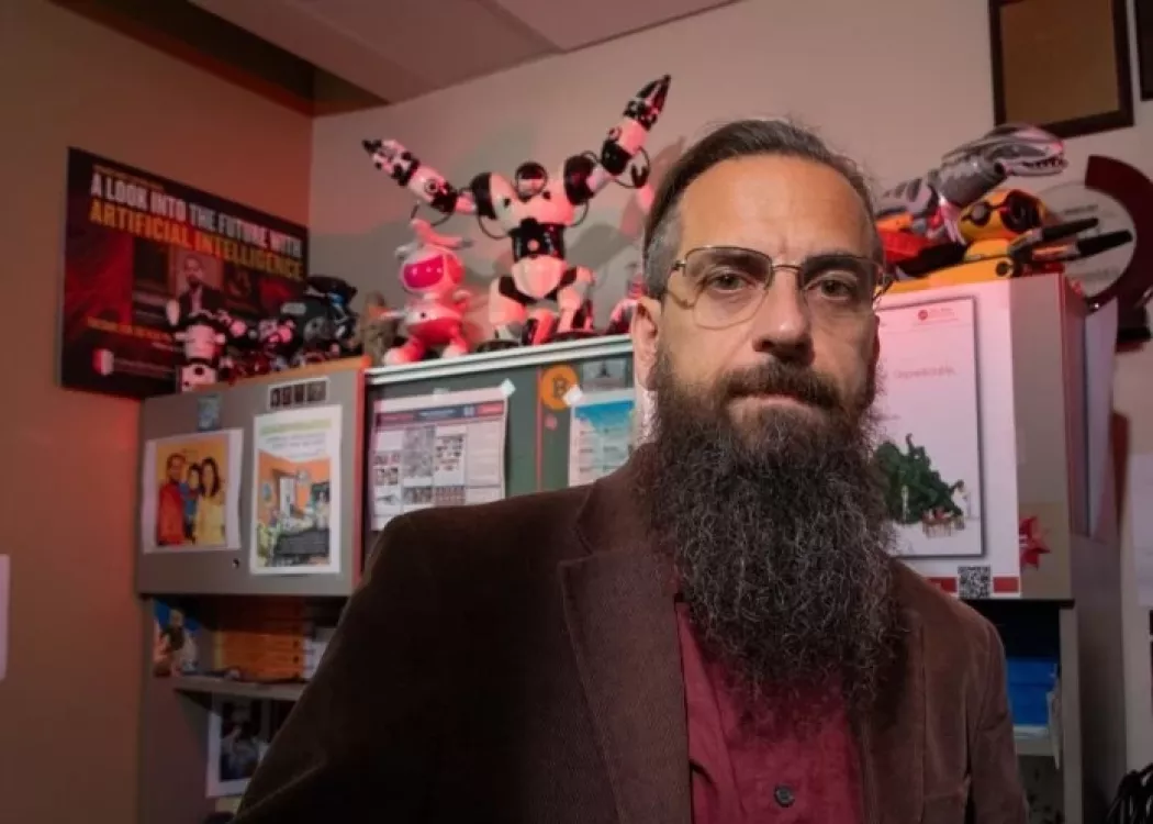 Roman Yampolskiy posing in his office, which is filled with toy robots and posters related to AI.