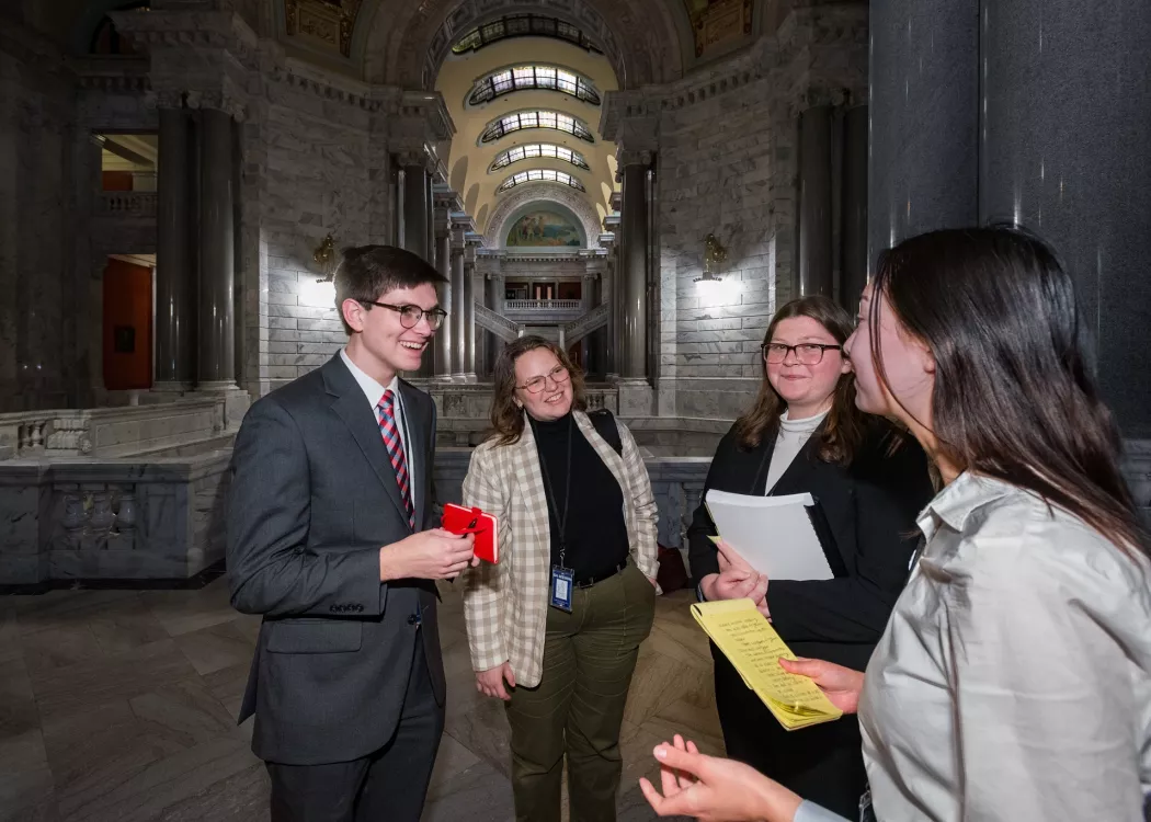 three young women and one young man all dressed professionally gather in a hallway in a government building