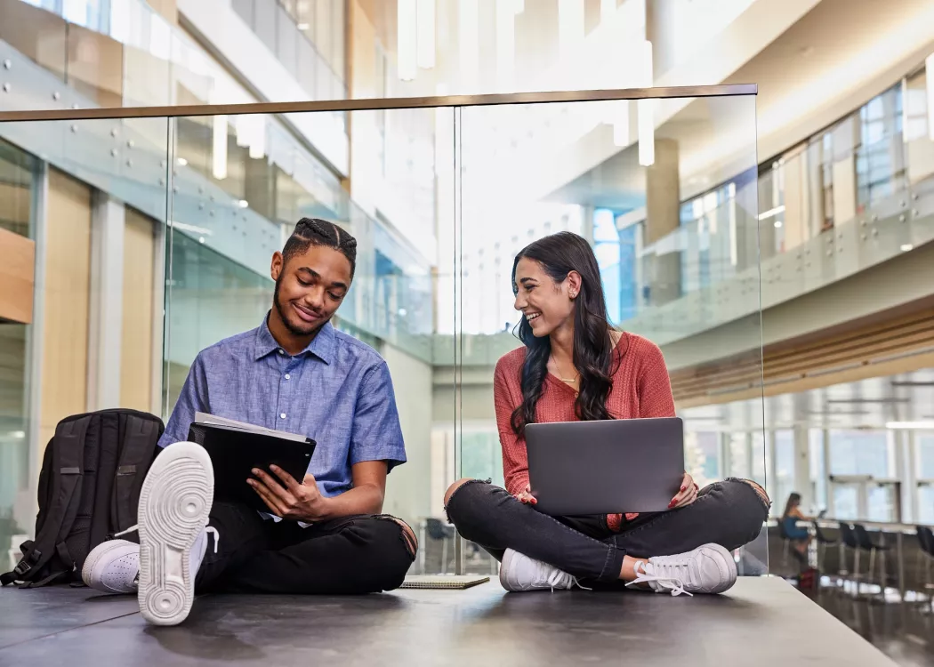 Two students are sitting on the floor while they study and do academic research on the second floor of the Belknap Academic Building.