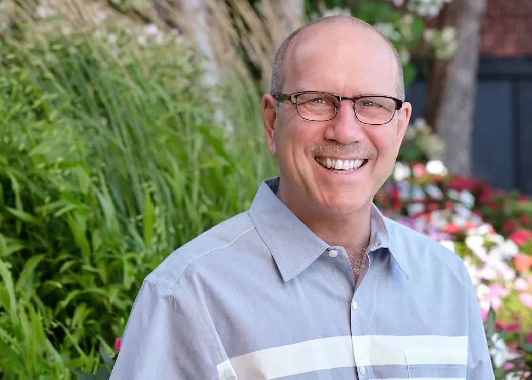Head shot of a man standing in front of greenery