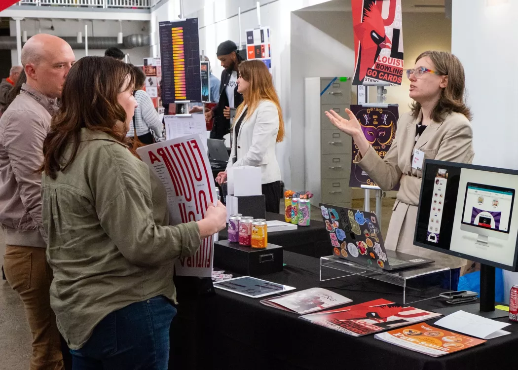A student talks animatedly as someone holds one of their posters at a showcase.