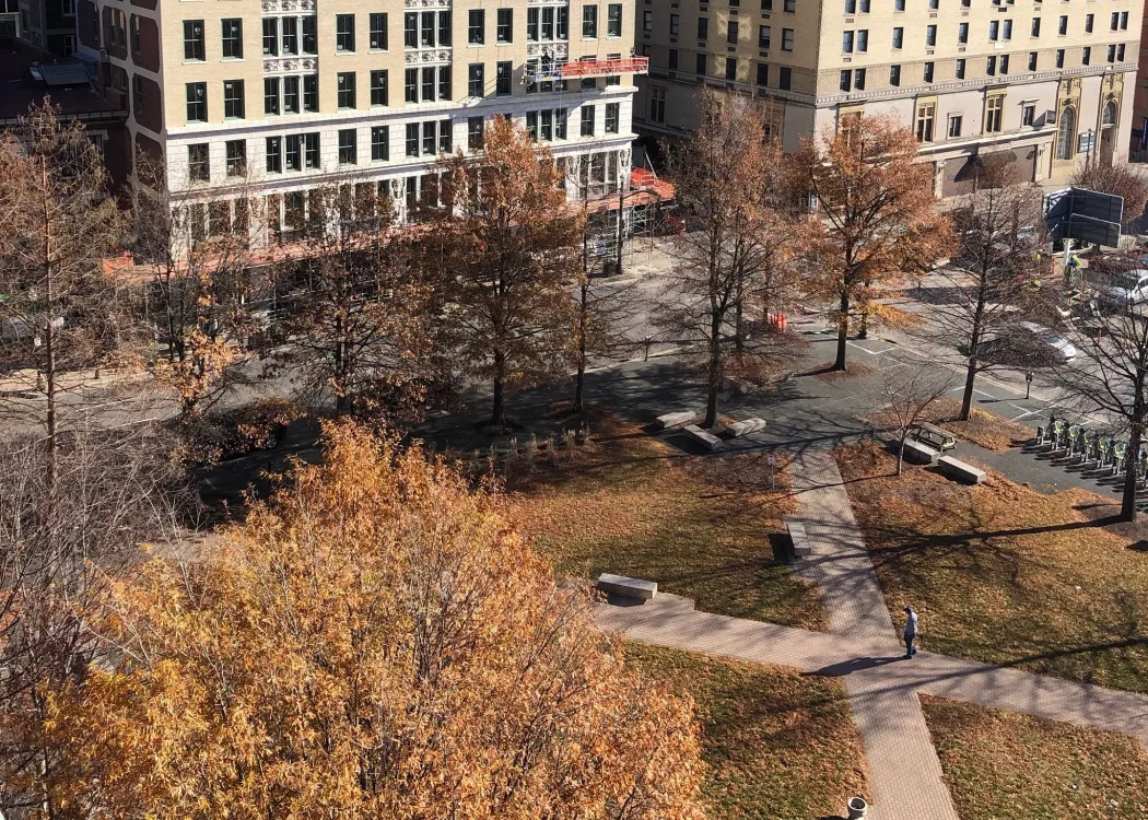 Overhead view of small park with sidewalks and trees. Office buildings are visible across the street.