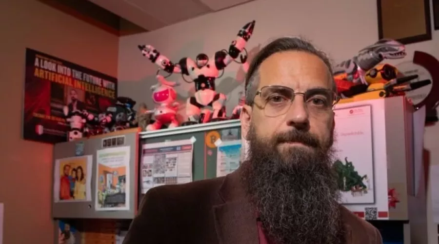 Roman Yampolskiy posing in his office, which is filled with toy robots and posters related to AI.