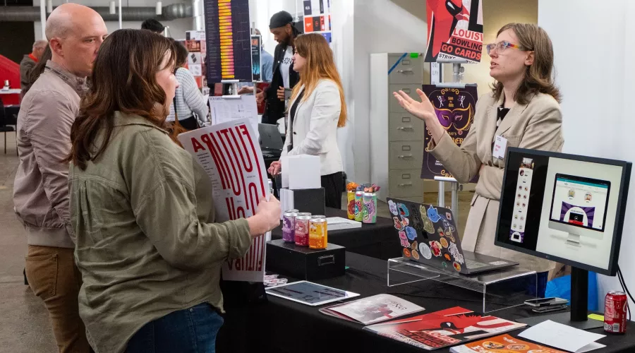 A student talks animatedly as someone holds one of their posters at a showcase.